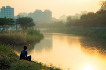 Silhouette of individual by serene river at sunrise, reflecting