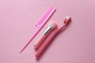 Toothbrush, comb and makeup brush on pink background