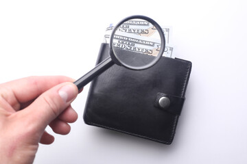 Hand with a magnifying glass examines a hundred dollar bills in purse