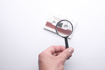 Hand with a magnifying glass examines retro audio cassette