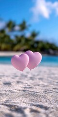 Fototapeta premium Two pink heart-shaped balloons on sandy beach with a beautiful blue ocean backdrop.