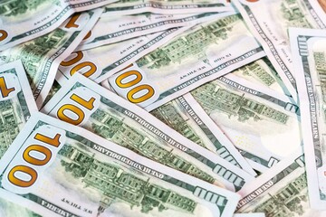 Pile of hundred dollar bills scattered on a surface in an indoor setting during daytime