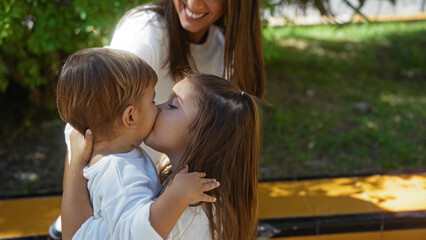 Woman smiling at her young son and daughter sharing a loving moment in an outdoor urban park setting, highlighting family togetherness in a vibrant city environment.