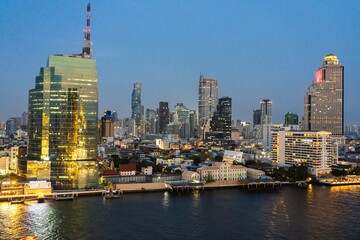 Obraz premium Stunning skyline view of Bangkok illuminated at dusk showcasing modern architecture along the river