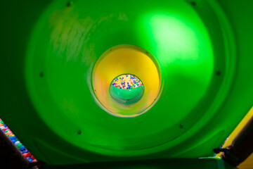 A thrilling perspective from inside a green tunnel slide leading to a vibrant ball pit.