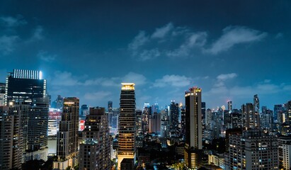 Naklejka premium City skyline illuminated by lights at night with clouds in the sky over urban landscape