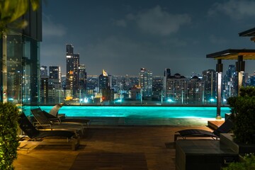 City skyline illuminated at night with rooftop pool and lounge chairs overlooking urban landscape