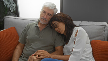 Fototapeta premium Middle-aged couple peacefully asleep on a cozy couch in a modern living room, reflecting comfort and togetherness in a warm home setting.