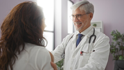 Fototapeta premium Doctor smiling at woman in clinic while discussing healthcare, showing warmth and professionalism in an indoor medical setting.