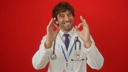 Man smiling in a white coat with stethoscope over isolated red background, conveying confidence and positivity in a healthcare setting.