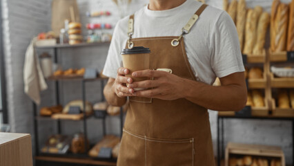 Man in an apron holding a coffee cup in a bakery with bread and pastries displayed in the background