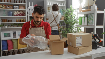 Men working together in a home decor shop, one packing items carefully in boxes while the other arranges shelves in the store interior.