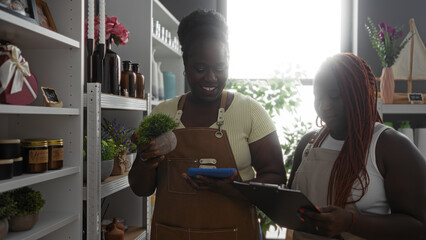 African american women employees working in a home decor store, checking inventory with digital devices among shelves of decorative items.