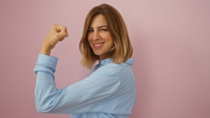 Attractive young woman smiling confidently with a strong arm pose over an isolated pink wall...