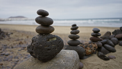 Stacked stones on the sandy famara beach in lanzarote, canary islands, depicting tranquility and balance during daylight with ocean waves in the background.