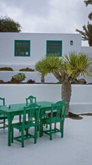 Outdoor green chairs and tables in lanzarote patio with white walls, palm trees, and windows during daylight