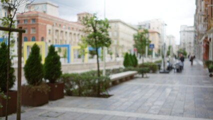 Fototapeta premium Blurred view of an urban street in la spezia, italy with bokeh effects, benches and trees lining the walkway under a cloudy sky.