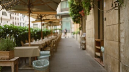 Fototapeta premium Blurred view of a cozy outdoor cafe on a charming street in rome, italy, showcasing defocused tables and umbrellas under a bright sky.