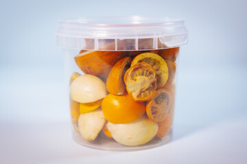 A clear plastic container filled with freeze-dried tomatoes of various colors and cuts. Vibrant orange and yellow tones dominate. Ideal for long-term storage and culinary uses.