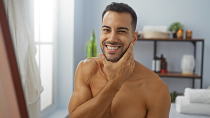 Handsome young man with a beard smiling in a spa room touching his face showcasing beauty and...