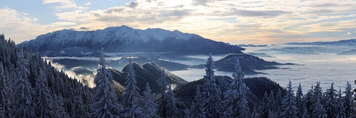 Bucegi mountains panorama view with forest and sea of ​​clouds below, during a beautiful winter day. Travel, massive fresh snow. 
