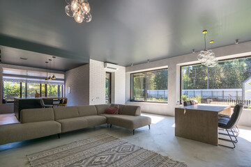 The interior of a spacious living room of a country house with panoramic windows and a beautiful view of the summer landscape.