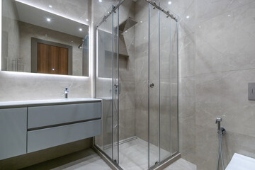 The bathroom has a modern touch shower behind glass sliding doors. The room is decorated with light gray tiles.