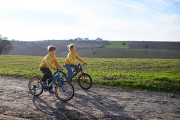 Obraz premium A boy and a girl race their bicycles through the countryside at sunset, laughing and chasing each other. The golden light and peaceful surroundings create a joyful, carefree moment of childhood advent