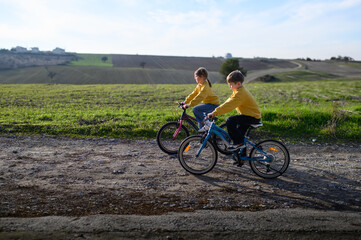 Obraz premium A boy and a girl race their bicycles through the countryside at sunset, laughing and chasing each other. The golden light and peaceful surroundings create a joyful, carefree moment of childhood advent
