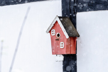 A small red birdhouse with white trim sits on a wall