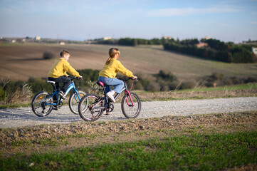 Obraz premium A boy and a girl race their bicycles through the countryside at sunset, laughing and chasing each other. The golden light and peaceful surroundings create a joyful, carefree moment of childhood advent