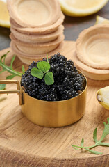 Black sturgeon caviar in copper bowl, lemon wedges and empty tartlets on table