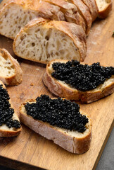 Sandwiches with black caviar served on a wooden board, top view