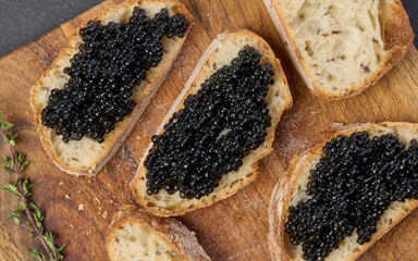 Sandwiches with black caviar served on a wooden board, top view