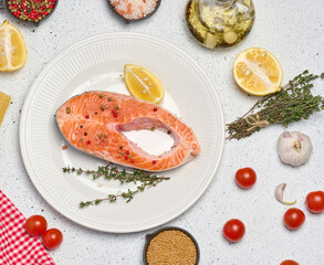 Raw piece of trout in white round plate and lemon slice, white background with spices. Top view
