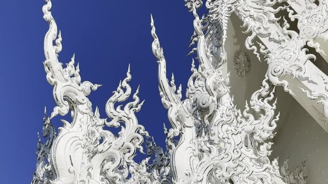 Close-up of the intricate white carvings on Wat Rong Khun&rsquo;s ubosot in Chiang Rai, Thailand. The ornate patterns stand out against the clear blue sky.
