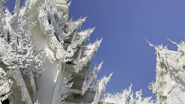 A close-up of the intricate white carvings on Wat Rong Khun, a famous tourist attraction in Chiang Rai, Thailand. The detailed patterns reflect Thai craftsmanship, set against a vibrant blue sky.