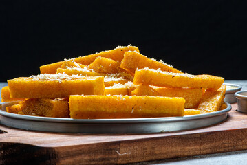 Porção de polenta frita com parmesão ralado servida sobre tábua de madeira