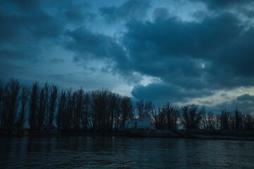 Obraz premium As the sun dips below the horizon, a tranquil river reflects the moody colors of dusk. Silhouettes of trees line the banks, creating an ethereal atmosphere