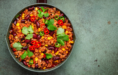 Chili con carne with minced beef, beans, paprika, corn, cilantro, jalapeno pepper in tomato sauce, tex-mex cuisine in green frying pan, top view