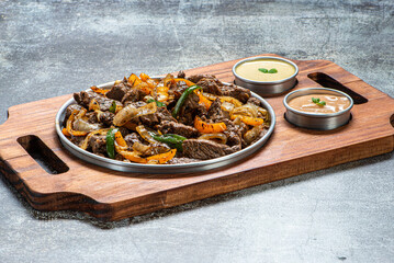 Porção de carne com cebola e pimentões, servida com molho de maionese e molho rose