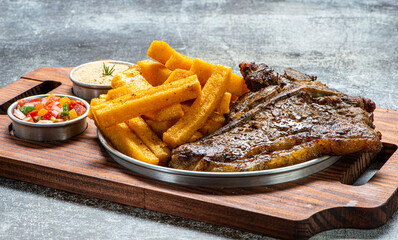 Carne grelhada servida com polentas fritas , farofa e molho vinagrete
