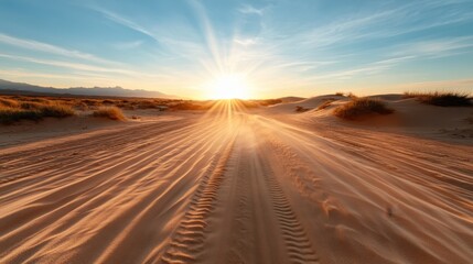 As the sun sets over the horizon, it casts a stunning glow over sandy trails marked by tire impressions, evoking an essence of adventure and the beauty of desolate landscapes.