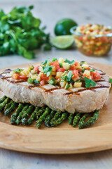 grilled swordfish topped with mango salsa served with asparagus on a wooden platter