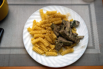 white plate featuring spiral pasta and sauteed beef liver garnished with fresh herbs, served on a dining table during lunch. Perfect for food related content