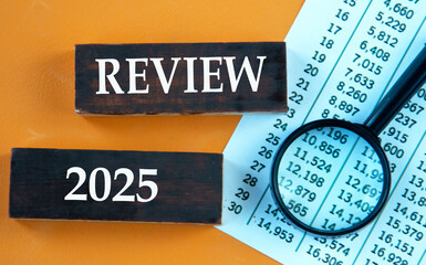 REVIEW 2025 - words on brown wooden bars against the background of a magnifying glass and a table...