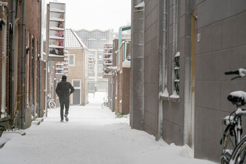 A man, seen from behind, walks along a snow-covered, narrow Dutch street. Creating a tranquil and picturesque scene in a charming snowy Netherlands town.