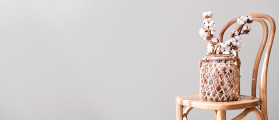 Vase with cotton flowers on chair against light background