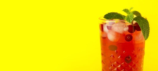 Glass of cold cranberry juice on yellow background with space for text, closeup