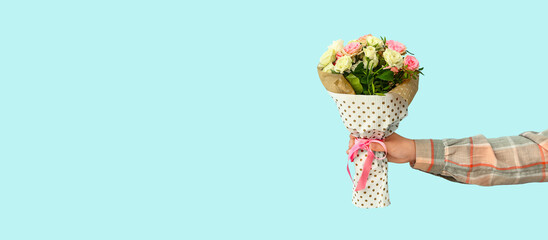 Hand of female florist with beautiful bouquet on color background